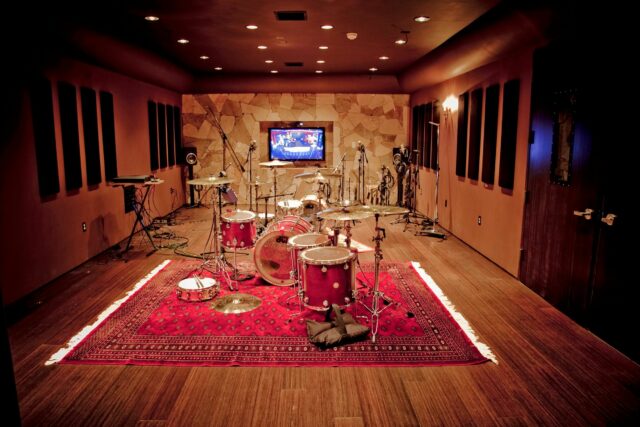 Red drums in recording studio with black acoustic panels on walls.