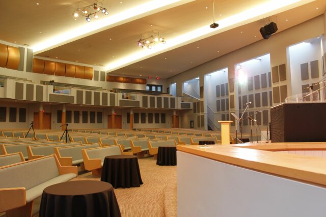 Empty church with tables in front of stage and grey acoustic panels on side and back walls.