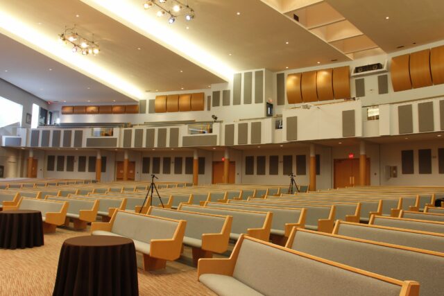 View of empty pews in church with grey acoustic panels on back wall