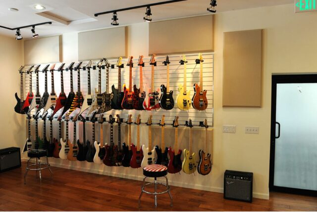 Wall with multiple guitars hanging along with beige acoustic wall panels