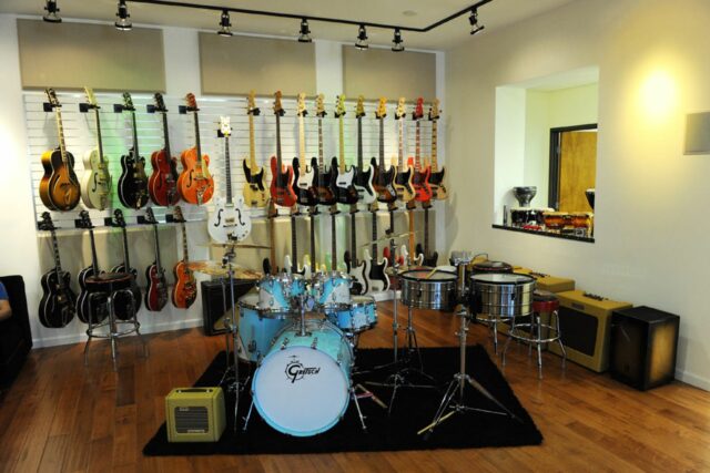 Light blue drum set with hanging guitars on wall with beige acoustic panels