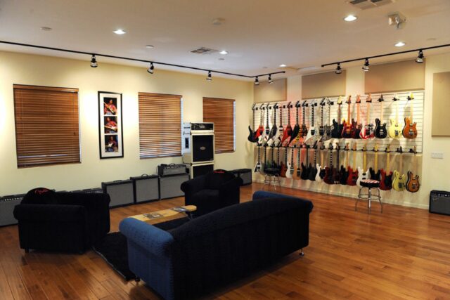 Black couch in guitar room with guitars and beige acoustic panels on walls.