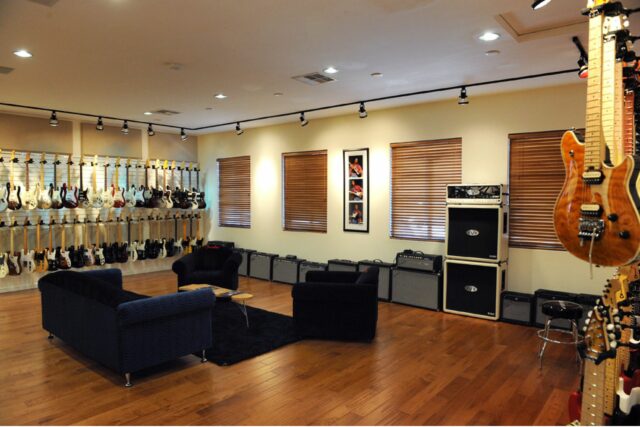 Black couch in middle of guitar showroom with beige acoustic panels on walls.
