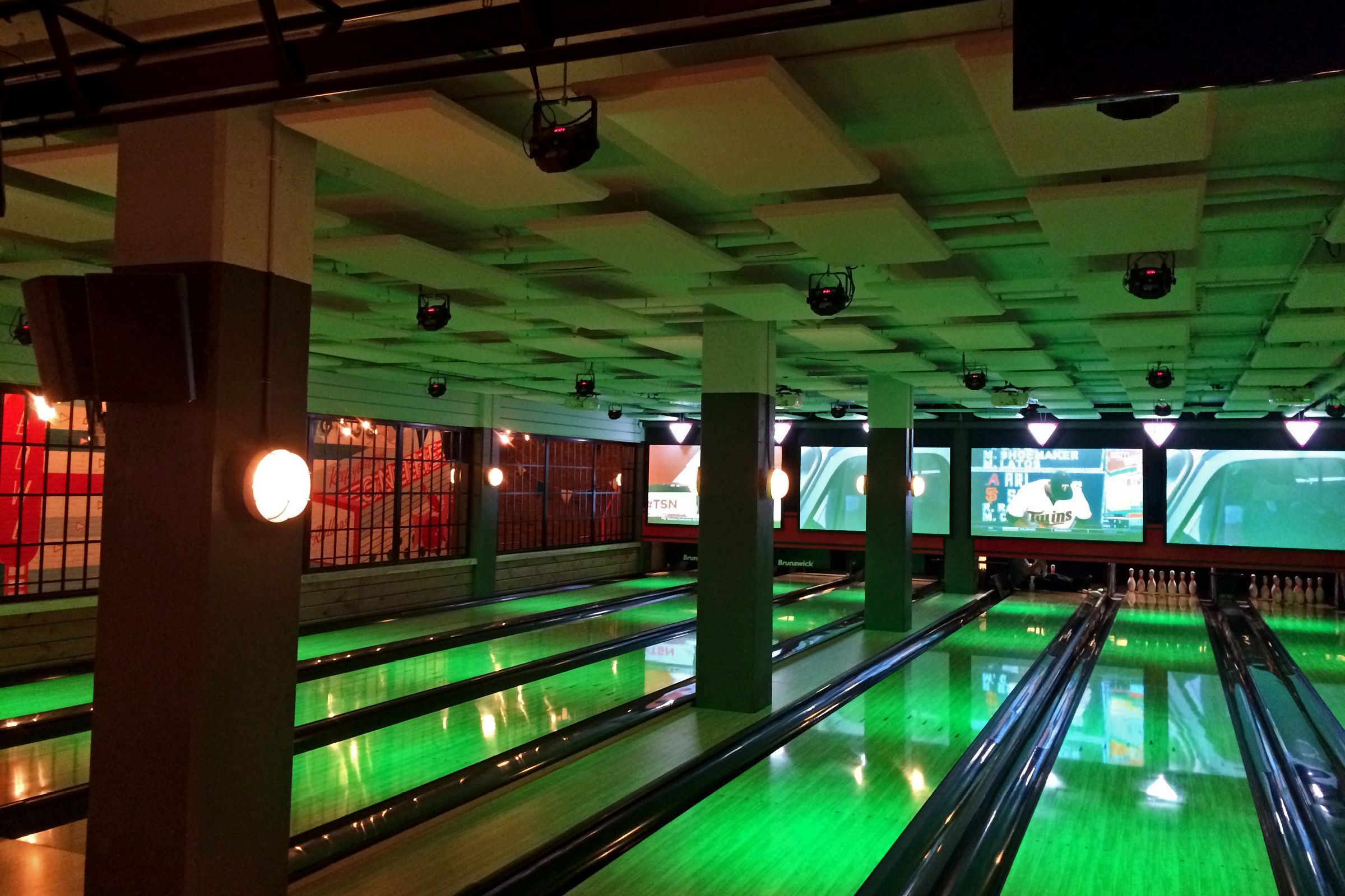 Bowling lanes with beige acoustic panels on ceiling above and green light shining