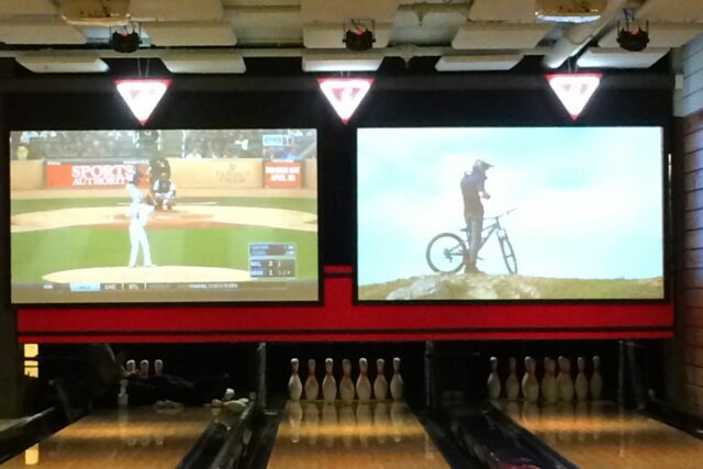 Bowling alley with two projectors on back wall and beige acoustic panels on ceiling