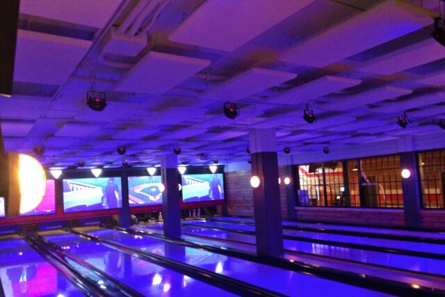 Bowling lanes with beige acoustic panels on above ceiling lit up by purple light