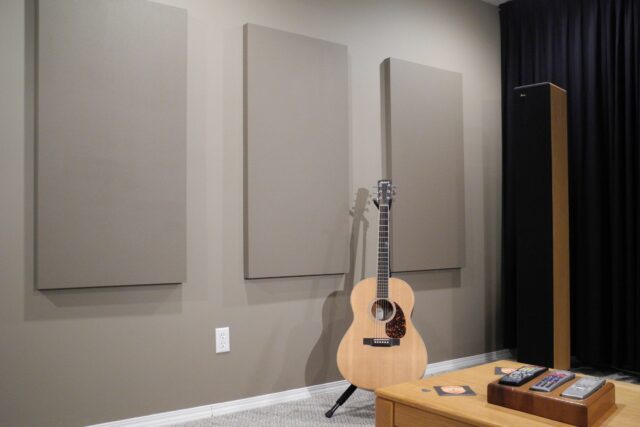 Grey wall with grey acoustic panels installed and acoustic guitar in front