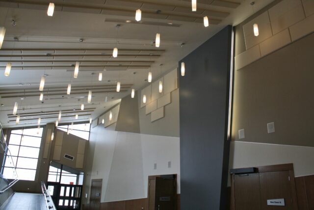 Conference centre with white walls, hanging lights, and high ceilings with acoustic panels installed.