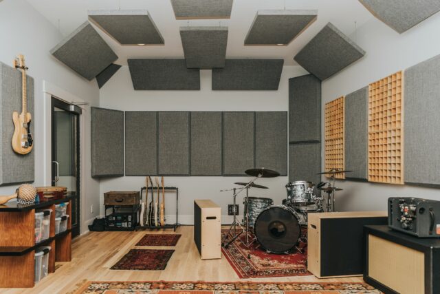 Several grey acoustic panels installed on walls and ceiling of recording studio with drums set up
