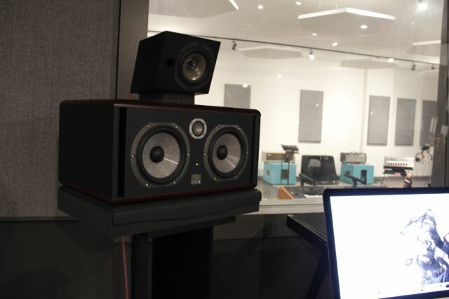 Black speaker with acoustically treated recording studio room in background