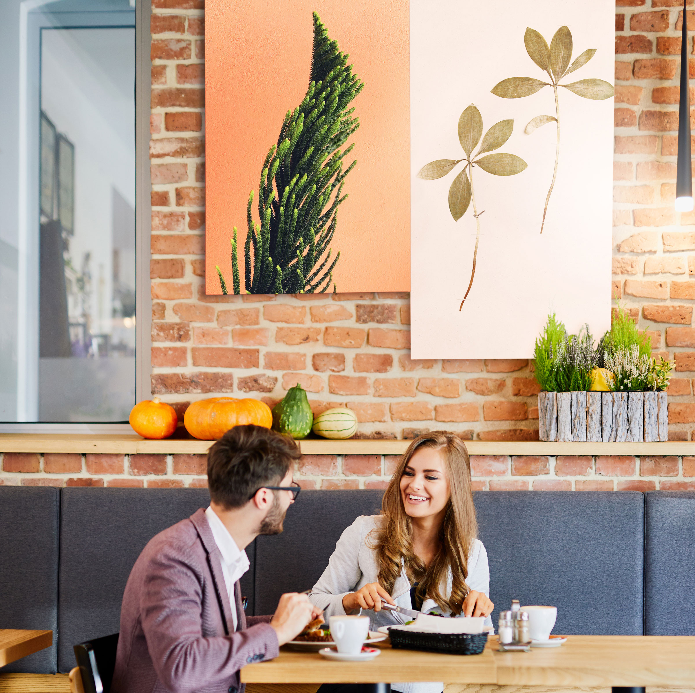 Man and woman sitting in cafe with custom painted acoustic panels hung on brick wall behind.