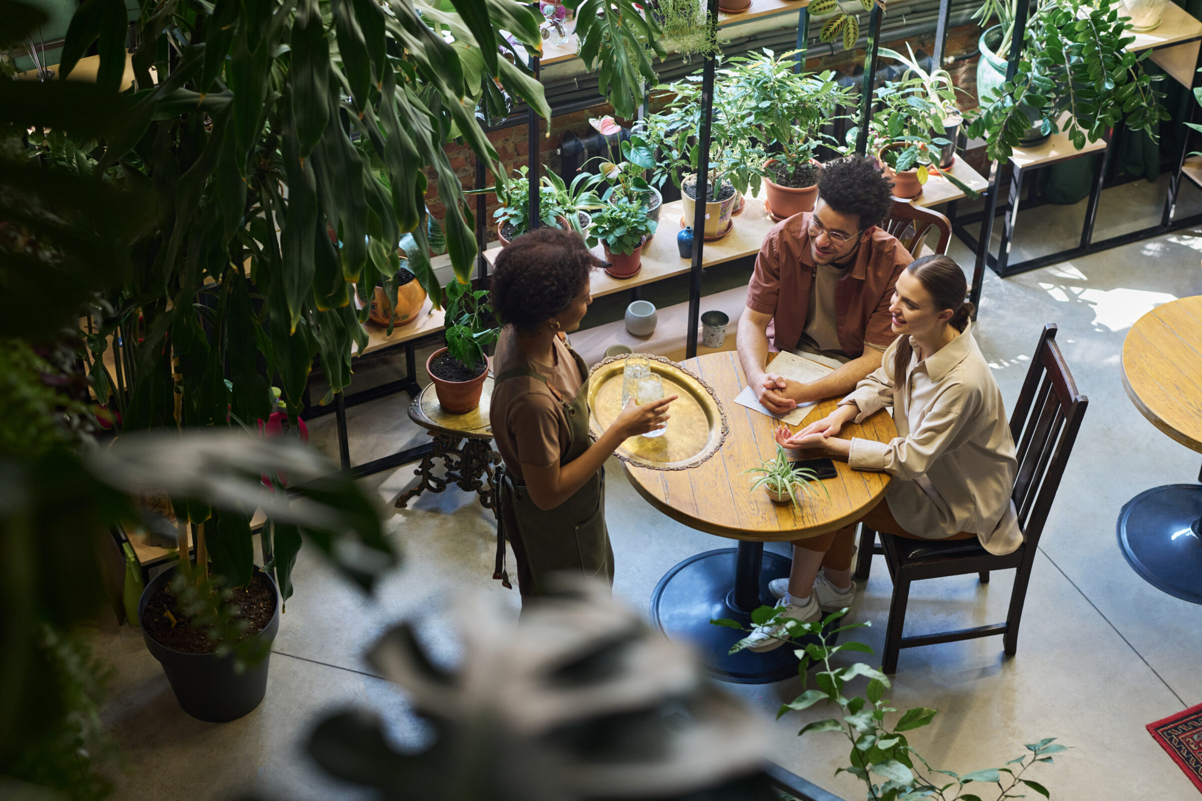 High Angle Of Young Intercultural Couple Looking At Waitress With Tray