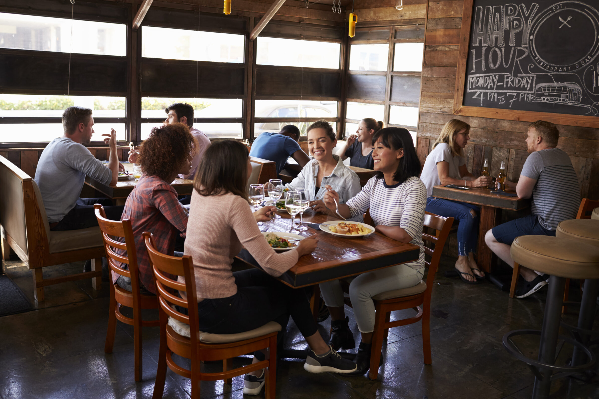 Four Female Friends At Lunch In Busy Restaurant, Full Length